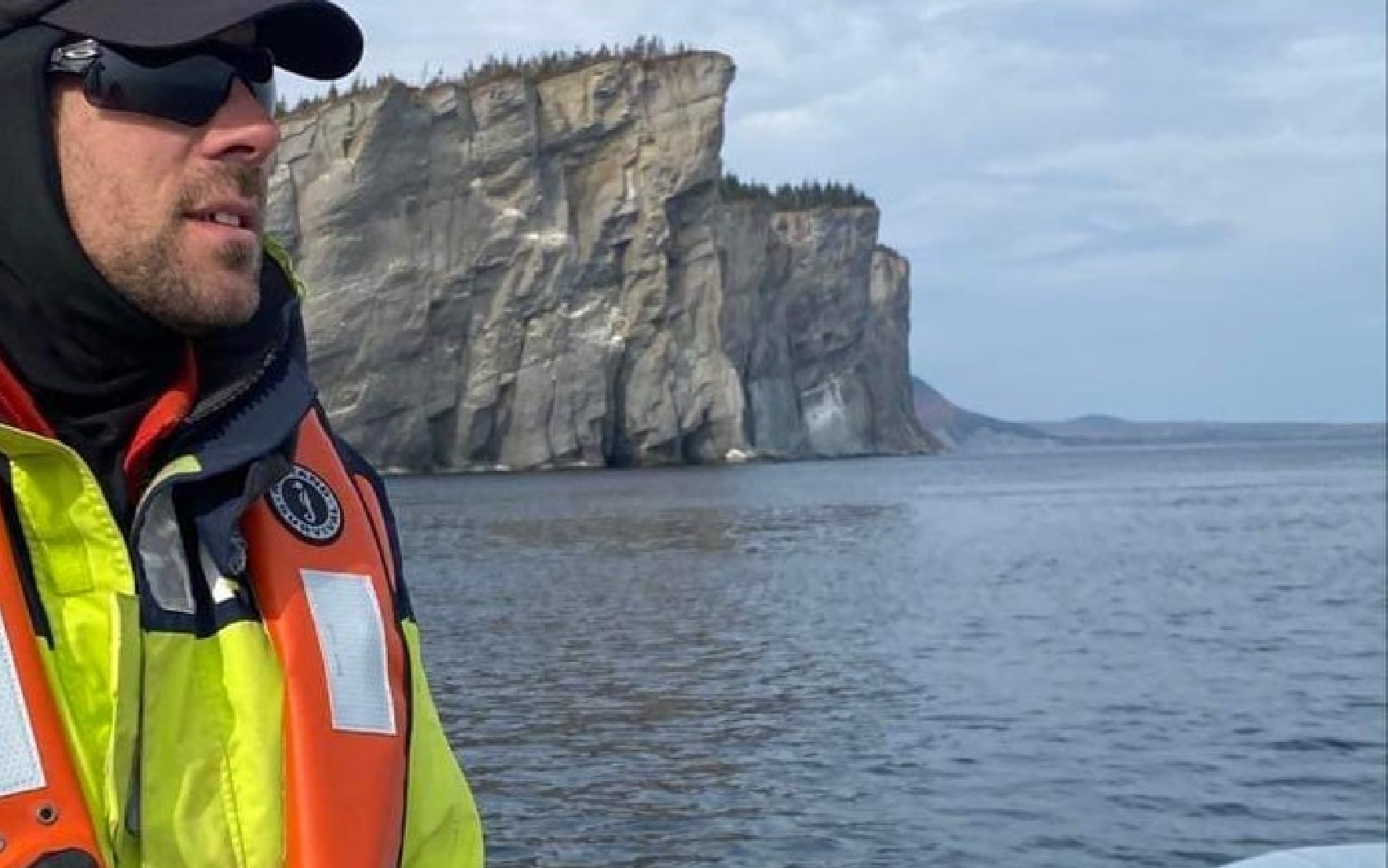 Guide-naturaliste à bord d’une embarcation devant les falaises du parc national Forillon en Gaspésie.